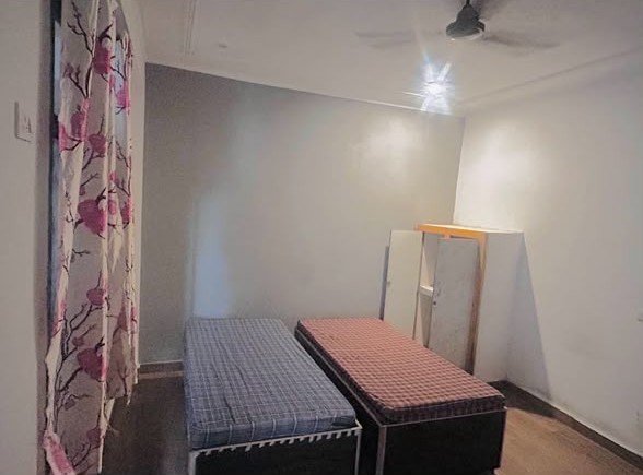 Non-AC room with two single beds, a wardrobe and a ceiling fan
